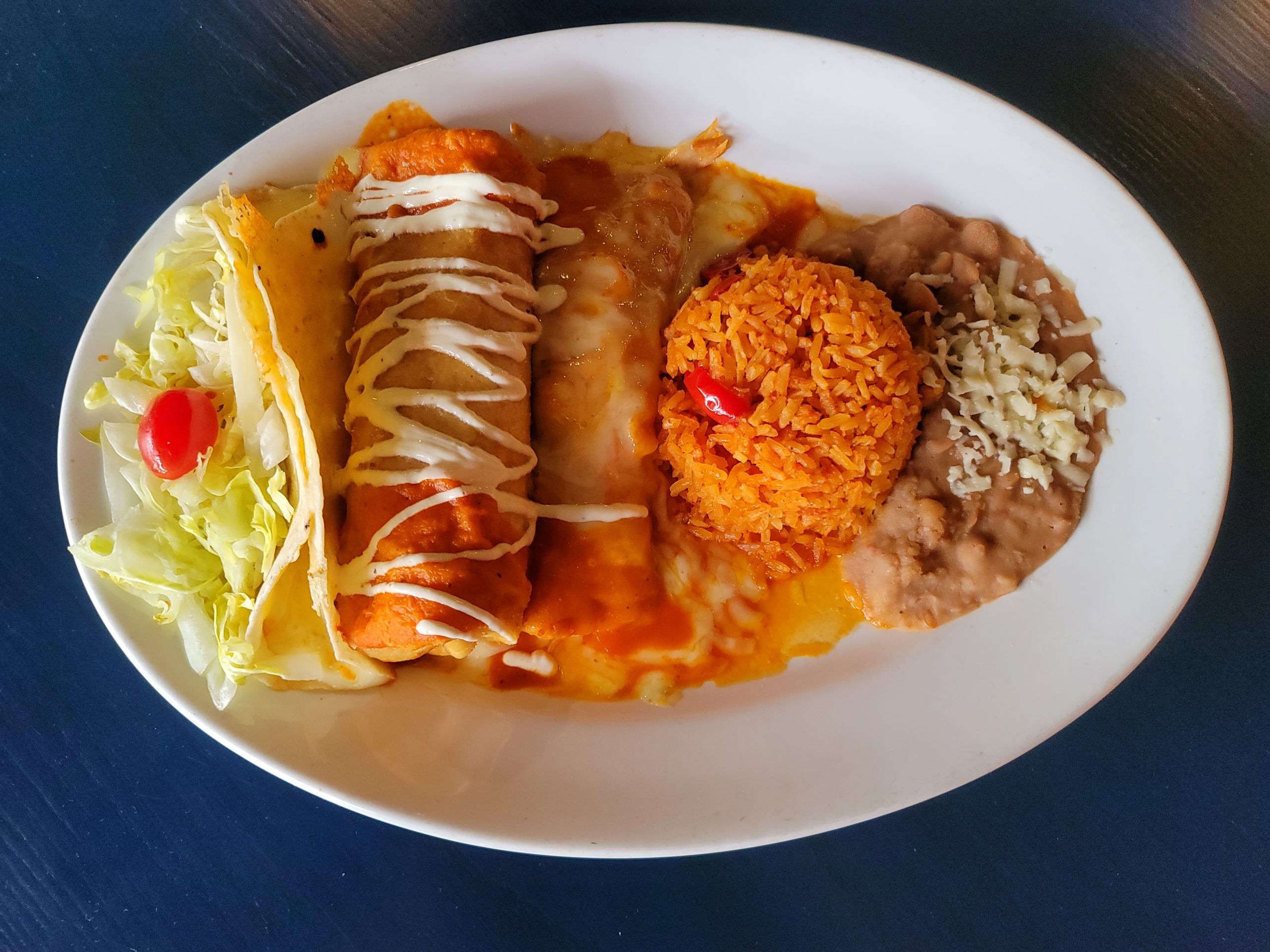 Dish called Combination 1 with Shredded Beef Chimichanga, Cheese Quesadilla and Chicken Enchilada with a side of Mexican Rice, Brown Beans and Small Salad, topped with sour cream and melted cheese